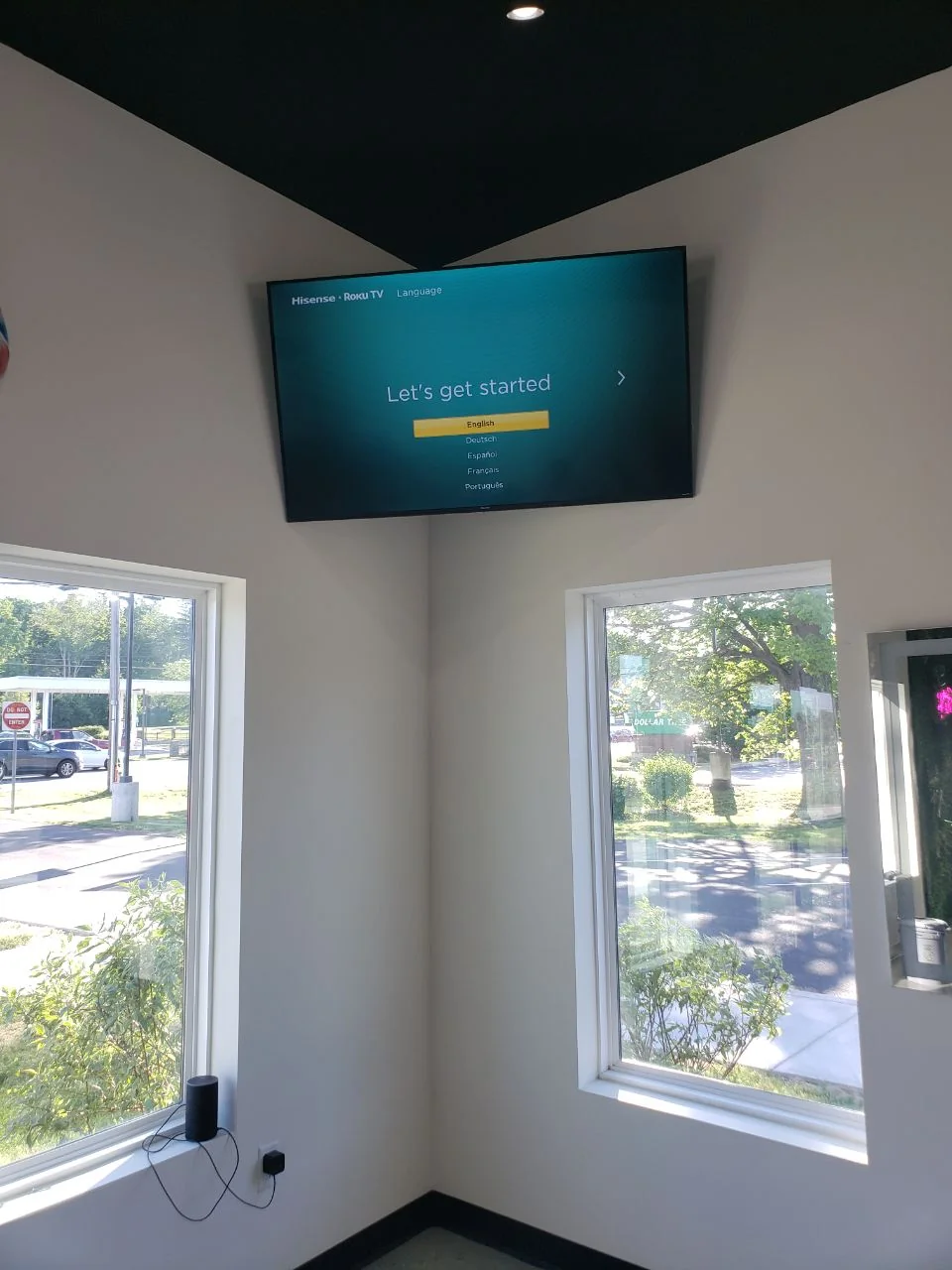Television mounted high on a wall above two corner windows.