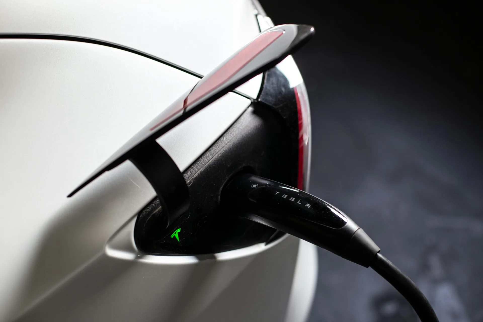 Charging connector plugged into the charging port of a white Tesla electric car.