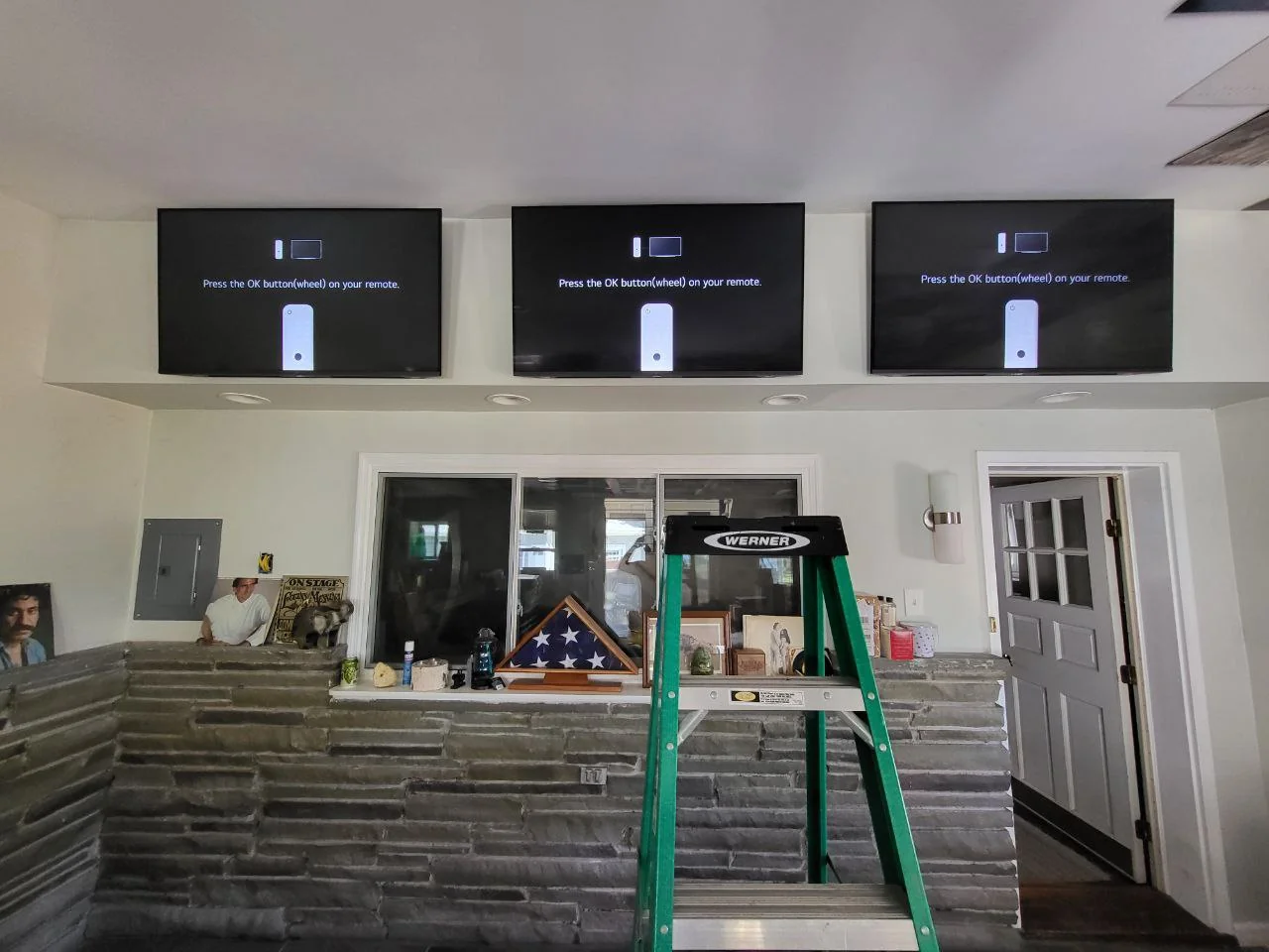 Three wall-mounted televisions above windows, with a ladder beneath them.