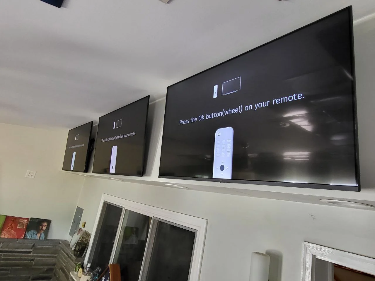 Close view of three televisions mounted high on a wall, displaying setup screens.
