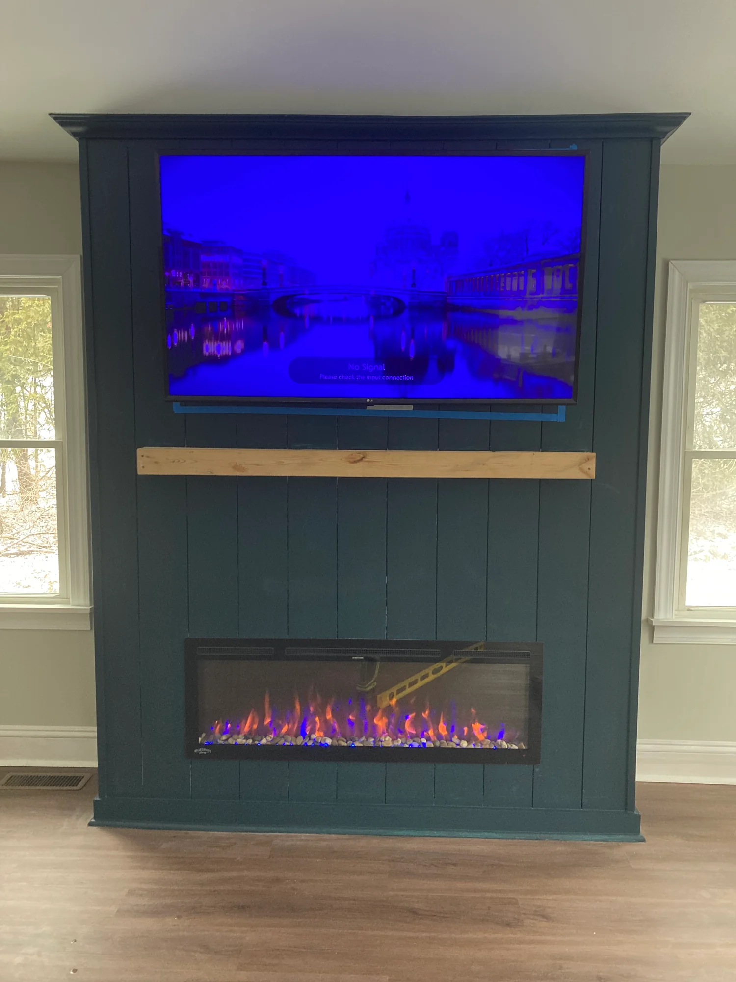 Television mounted above a linear electric fireplace in a dark paneled surround.