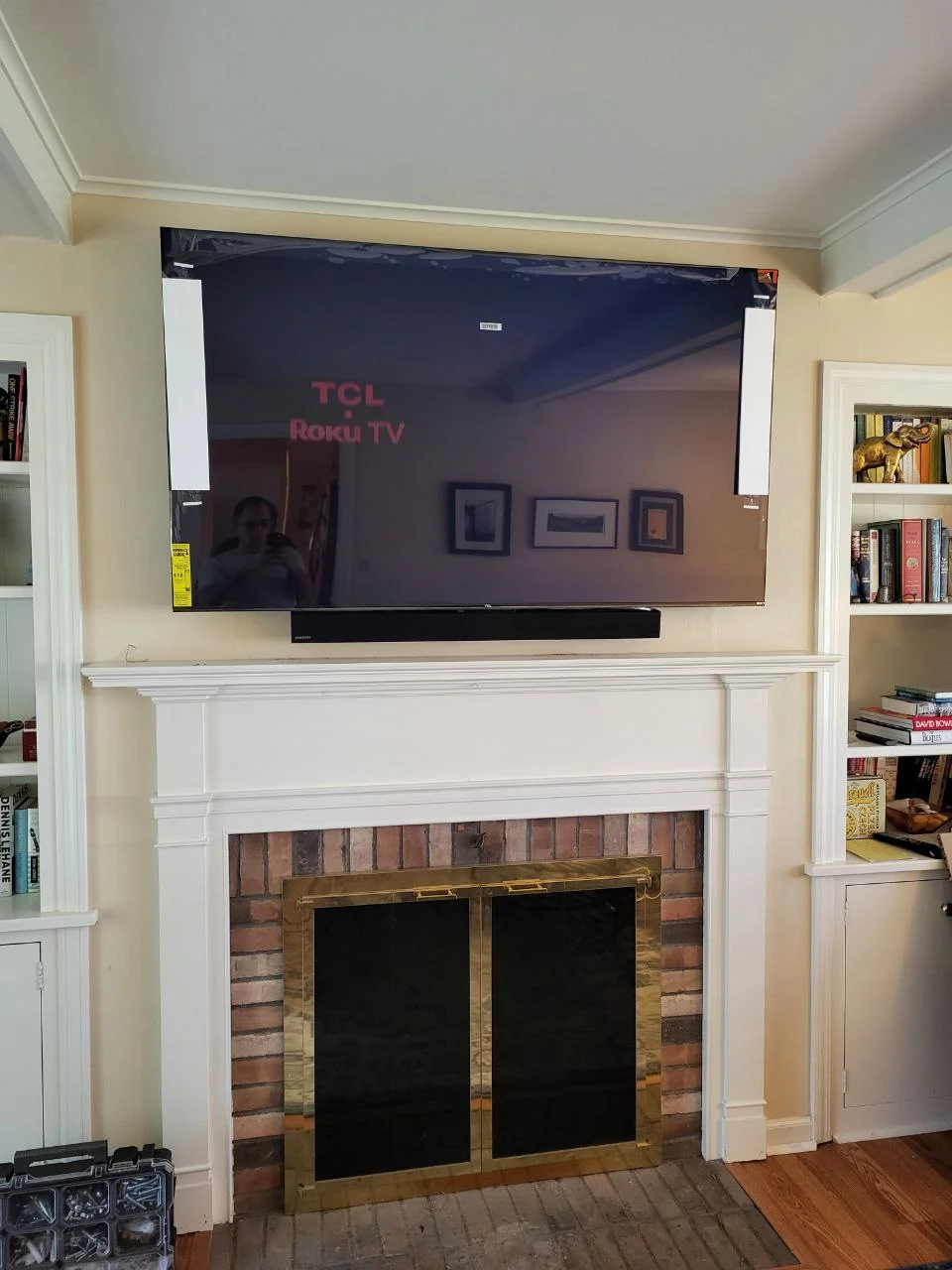 Television mounted above a white mantel and brick fireplace between built-in shelves.