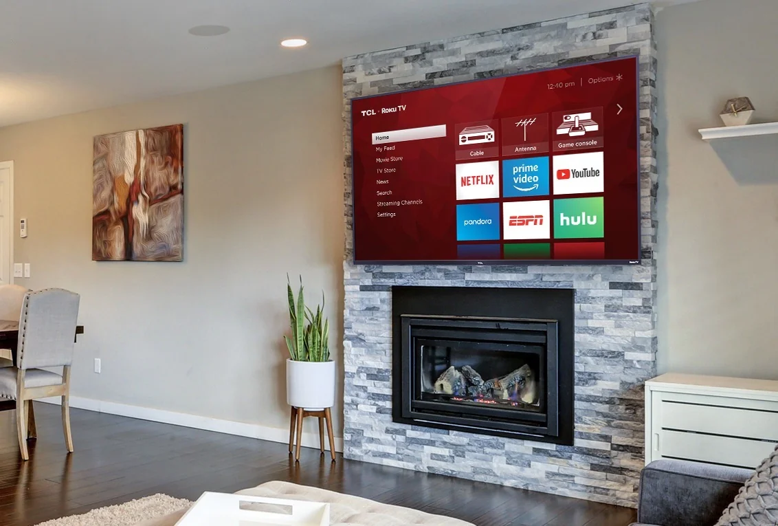 Television mounted above a stone fireplace, between white shelving and a window.