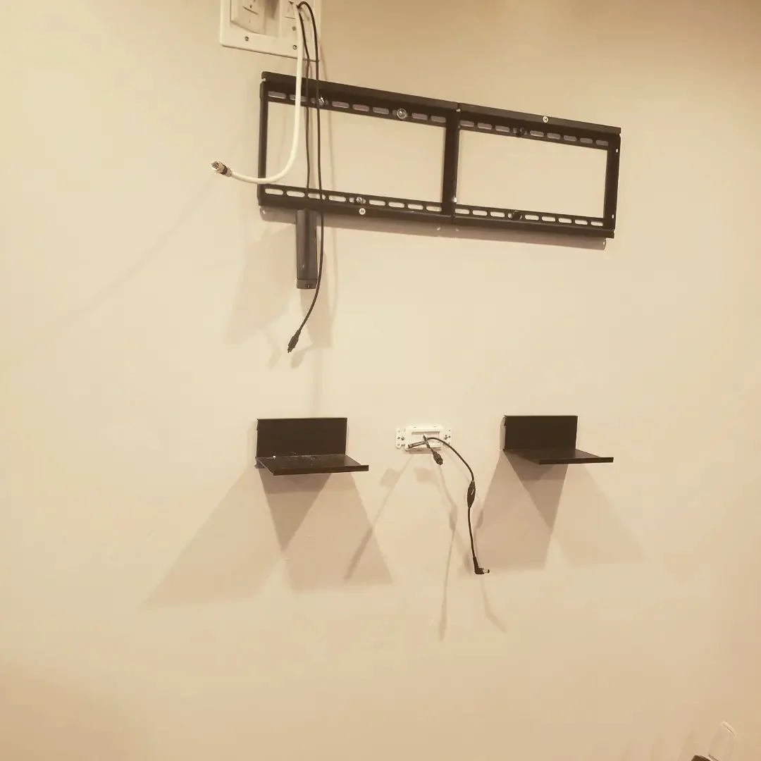 Empty television wall bracket above two small shelves, with cables hanging below.