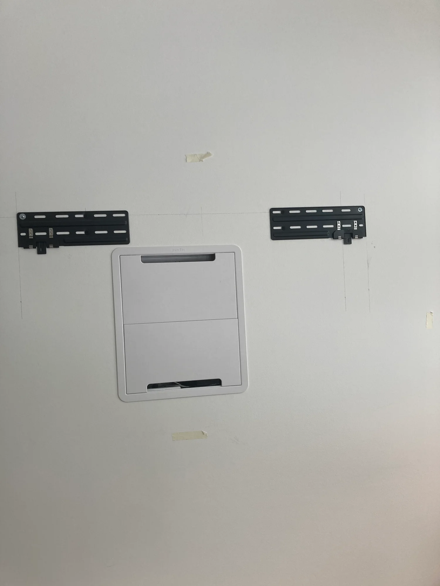 Two television mounting brackets on a white wall above a recessed box with its cover fitted.