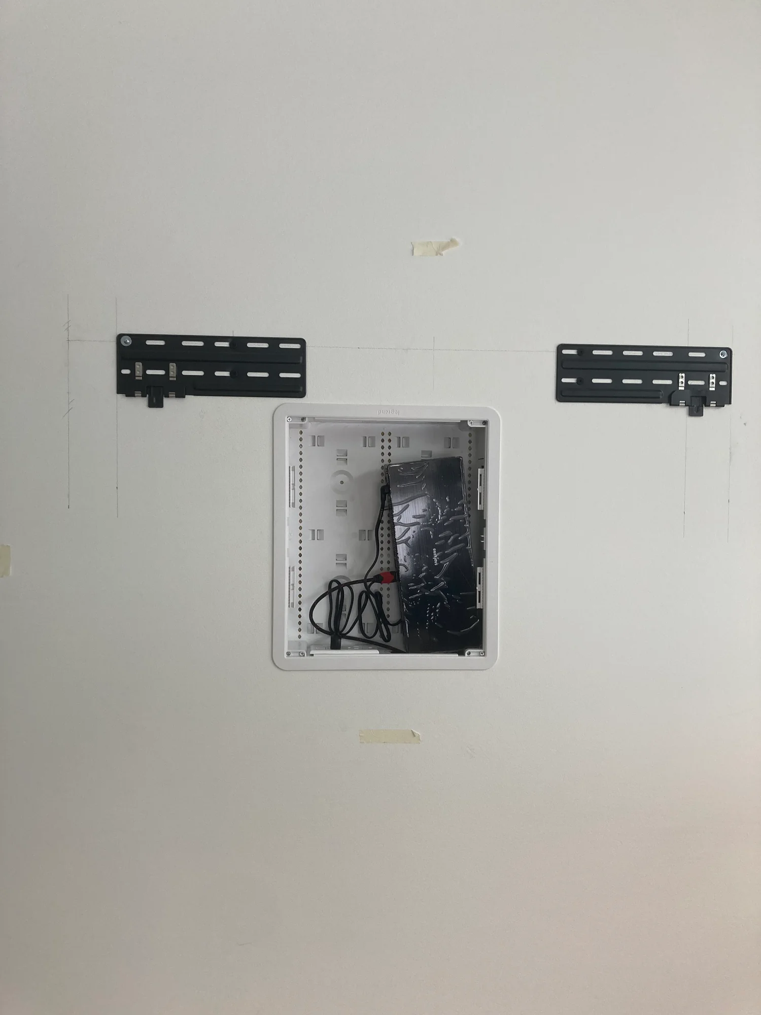 Two television mounting brackets on a white wall above an open recessed cable box.