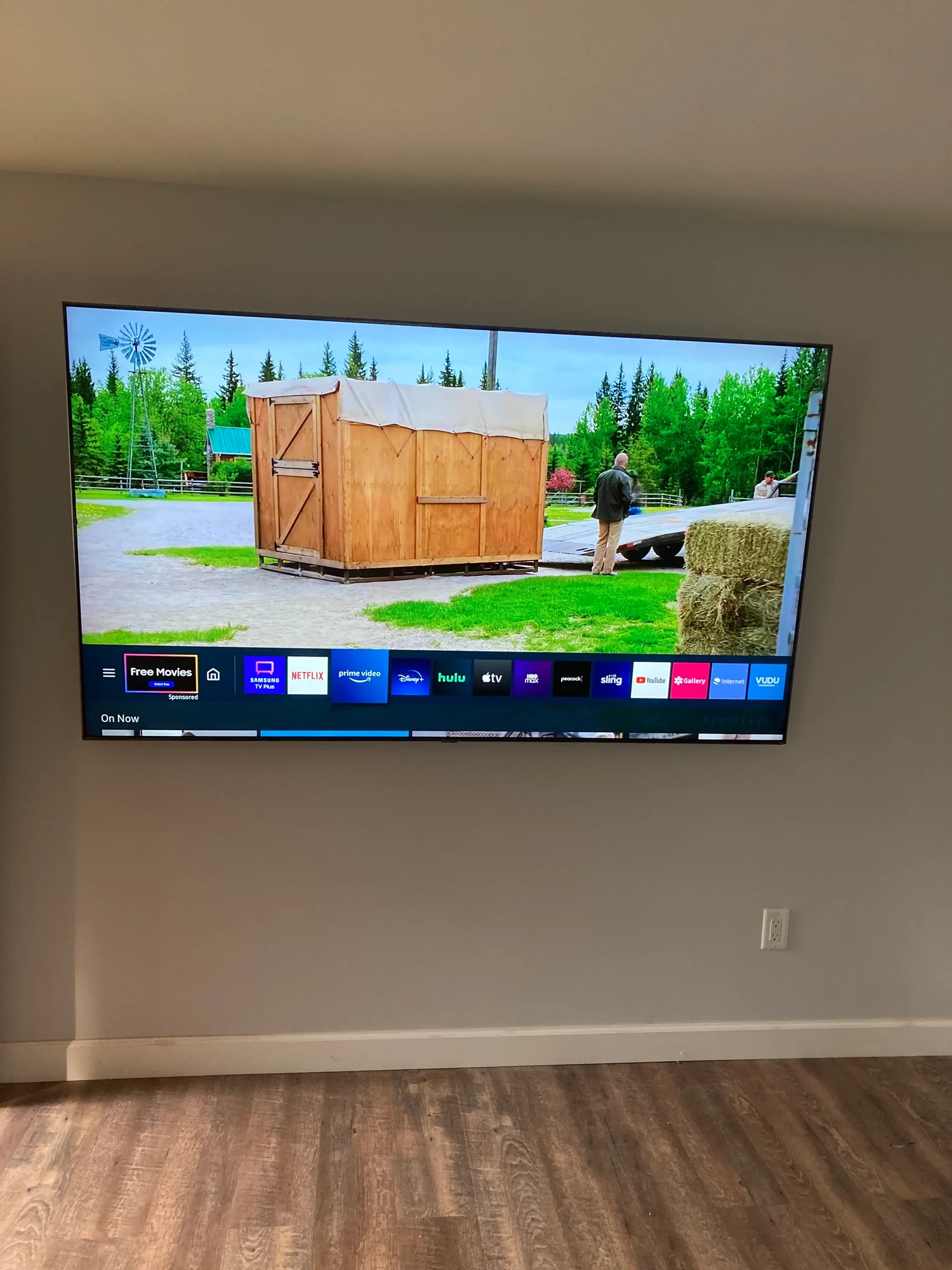 Television mounted on a gray wall above a hardwood floor, displaying a streaming menu.